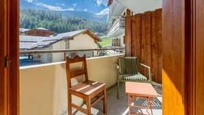 A balcony with a wooden chair, a green chair, and a small table.