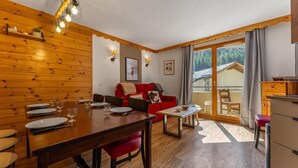 A wooden interior with a dining table set, a red sofa, and a view through a glass door.
