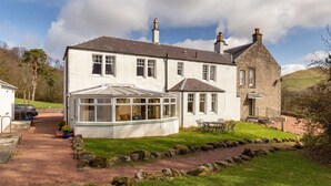 A two-story house with a conservatory, stone walls, and a garden with a gravel path and rocks.