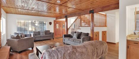 A spacious living room with wooden floors and ceiling, two grey sofas, a coffee table, and a staircase leading to another level.
