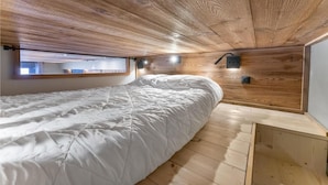Une chambre avec un plafond en bois, un lit, une fenêtre et un luminaire fixé au mur.