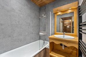 A modern bathroom with a bathtub, a wooden vanity with a sink, and a large mirror. - 40m from ski slopes, 1st floor, fitness, swimming pool, sauna, balcony, tv, ski locker, 35m² (Les Orres)