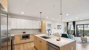 A modern kitchen with wooden cabinets, a stainless steel dishwasher, and a large island with a sink.