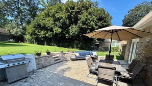 Une terrasse extérieure équipée d’un barbecue, d’un espace salon et d’un grand parasol.