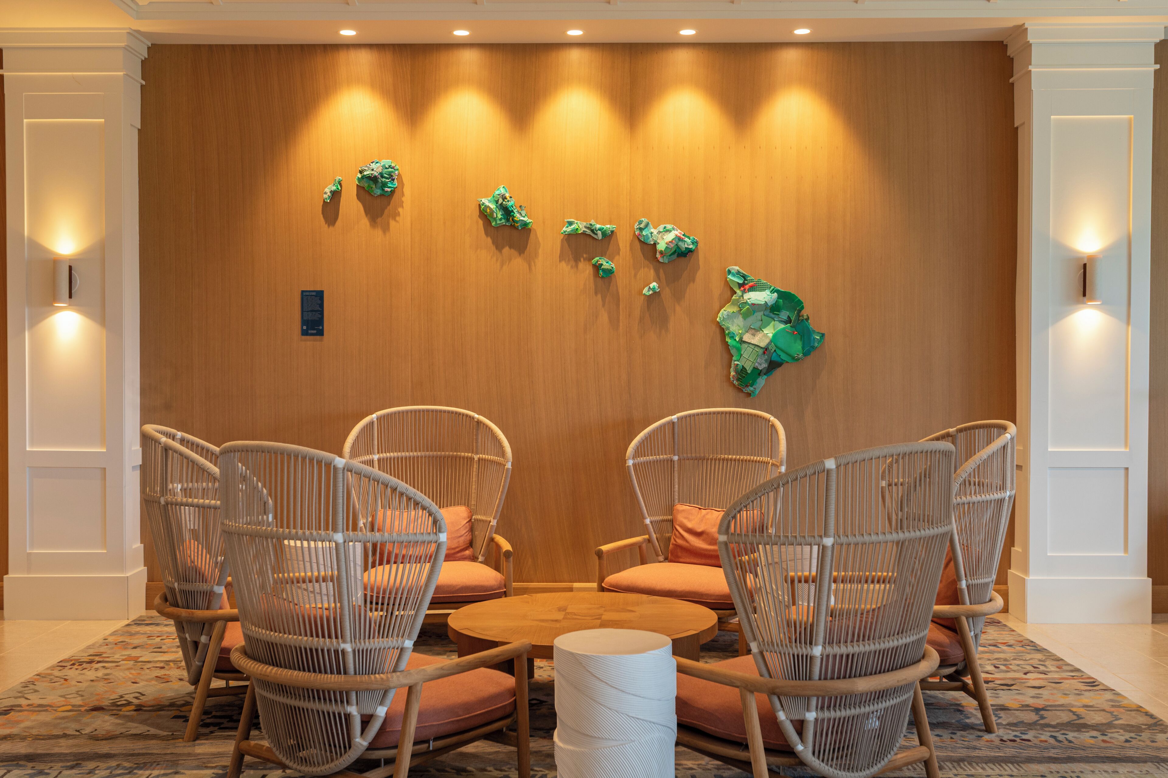 A room with wicker chairs, a round table, and a wooden wall with wall art.
