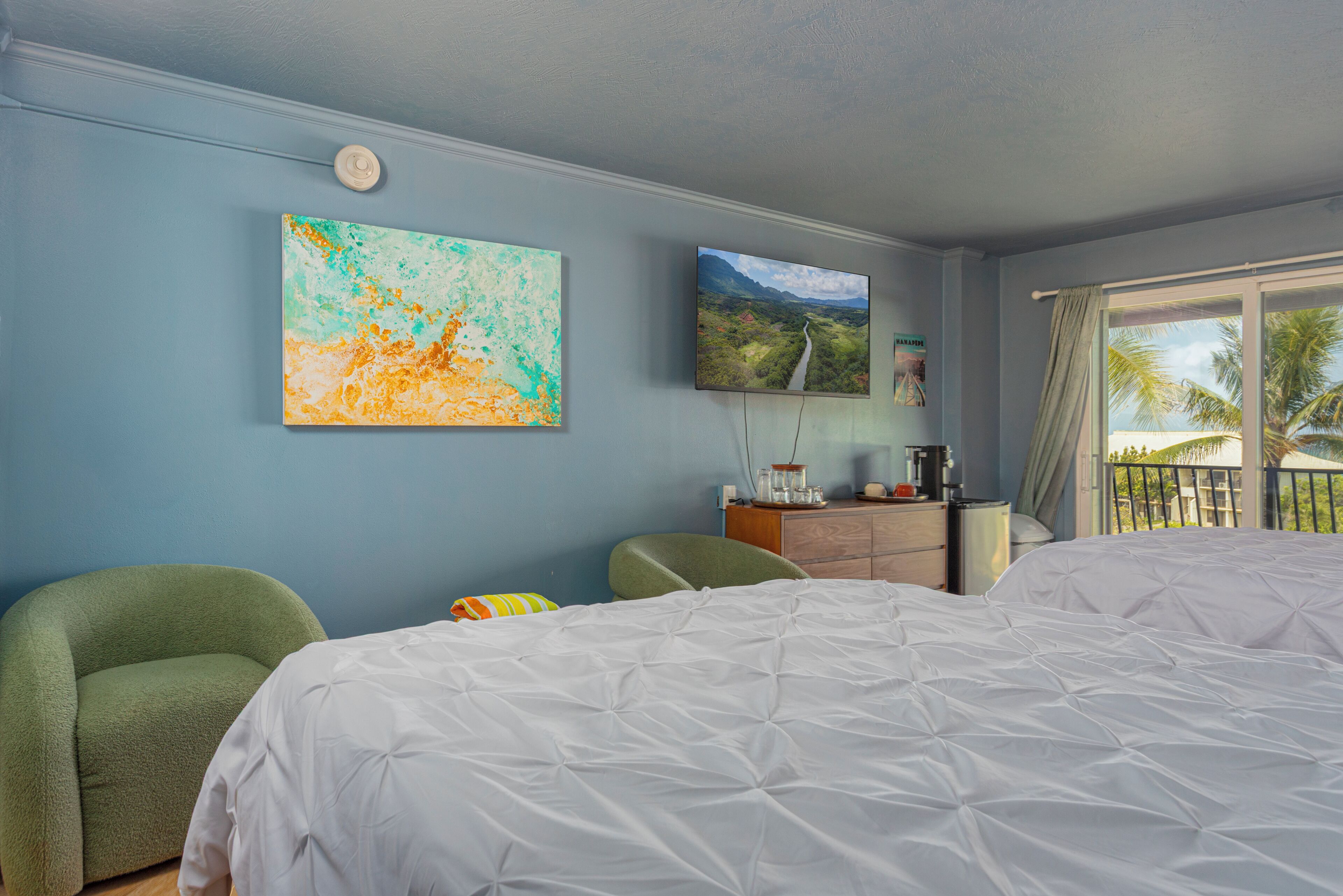 A hotel room with a bed, two chairs, a dresser, and artwork on the wall.
