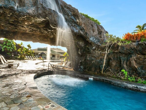 A pool area with a waterfall feature, lounge chairs, and a stone-tiled deck.
