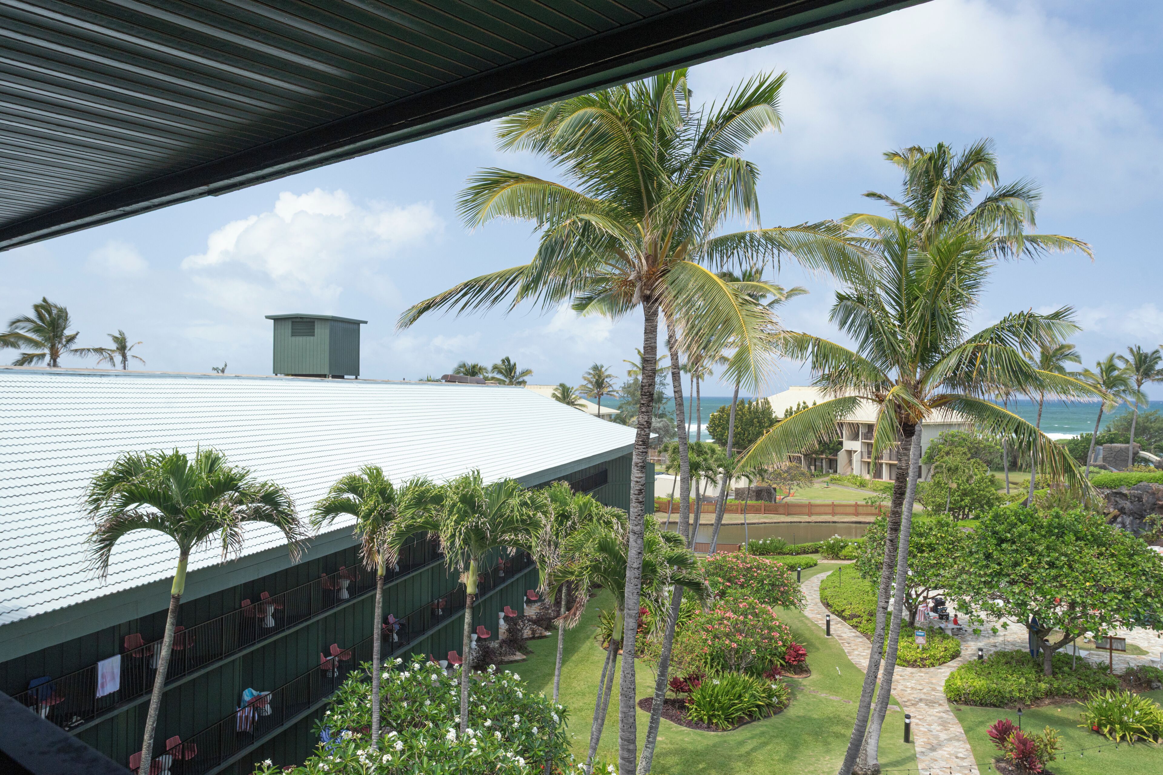 Un resort con una edificación techada, palmeras y vista al océano.