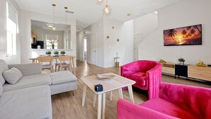 A modern living room with a sofa, a pink armchair, and a dining area with a table and chairs.
