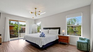 A bedroom with a large bed, a nightstand, a green chair, and a balcony with a view of the outside.