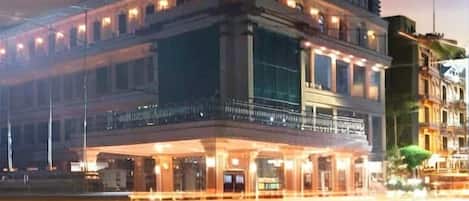 Un hotel de varios pisos con una imponente torre de reloj, amplias ventanas y una fachada bien iluminada.
