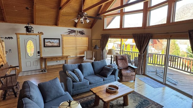 A spacious living room with a high ceiling, wooden beams, a large sofa, a coffee table, and a view of the outdoors through large windows.