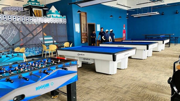 Un espace de loisirs équipé de tables de baby-foot, d’une table de billard et d’un baby-foot doté d’une enceinte grillagée.