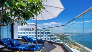 Eine Dachterrasse mit Liegestühlen und einem großen Sonnenschirm mit Blick auf eine Küstenstadt.