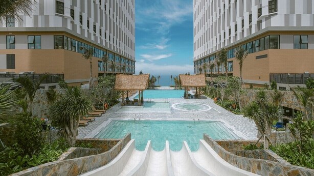 Ein modernes Hotel mit einem zentral gelegenen Pool, Liegestühlen und Palmen.