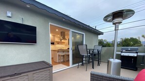 A patio area with a grill, outdoor seating, and a TV mounted on the wall. - Clean Penthouse with Balcony (Burbank)
