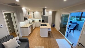 A modern kitchen with white cabinets, a central island, and a sliding glass door leading to an outdoor patio. - Clean Penthouse with Balcony (Burbank)