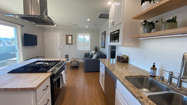 A modern kitchen with white cabinets, a granite countertop, stainless steel appliances, and a built-in oven. - Clean Penthouse with Balcony (Burbank)