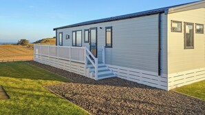 A single-story building with a white exterior, a covered porch with steps, and a view of the landscape. - Jura Premier Lodge with Hot Tub (Ayr)