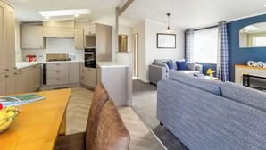 A compact living space with a kitchenette, a dining area, and a seating area with a sofa and a TV. - Jura Premier Lodge with Hot Tub (Ayr)