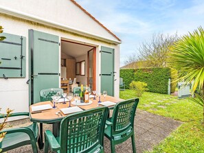 Un espace extérieur aménagé pour les repas, avec une table dressée pour quatre personnes, entourée de chaises vertes.