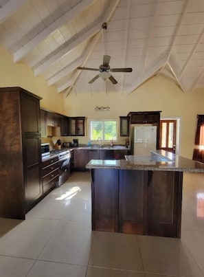 A spacious kitchen with dark wooden cabinets, a central island, and a ceiling fan. - Luxury Villa, Cades Bay, Nevis - Villa Tranquil (Cades Bay, St Thomas)