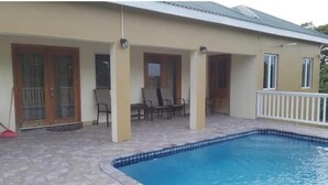 Una casa con piscina, un porche cubierto con sillas y una barandilla blanca.