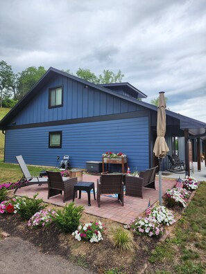 A blue house with a patio, outdoor furniture, and flower beds.