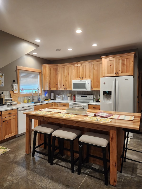 A modern kitchen with wooden cabinets, a central island with stools, a refrigerator, and a microwave.