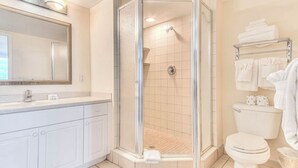 A modern bathroom with a glass-enclosed shower, white fixtures, and a vanity with a mirror. - Ocean View Charming condo at Daytona Beach (Daytona Beach)