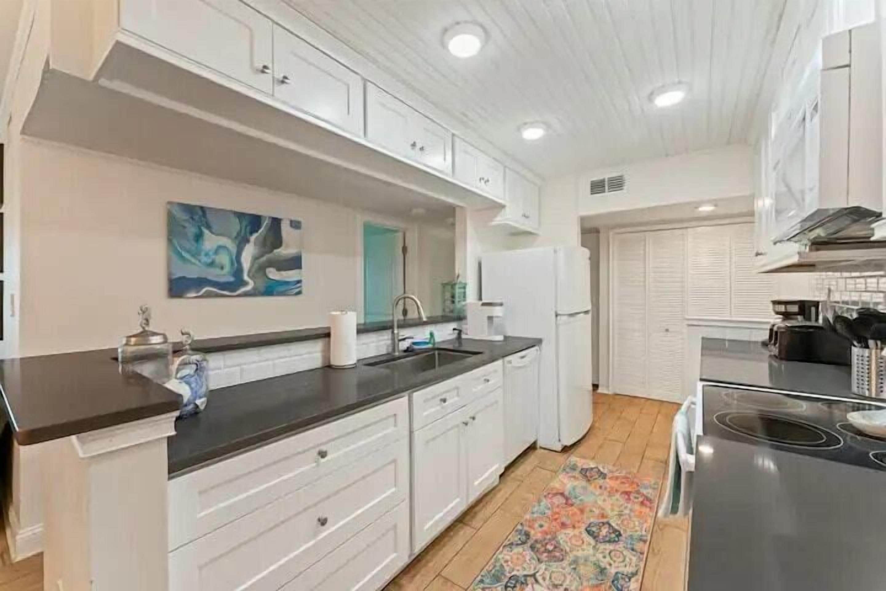 A modern kitchen with white cabinetry, a black countertop, and a colorful rug.