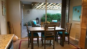 A dining area with a table and chairs, a kitchen area with a stove, and a view of the outdoors through a glass door. - SANDPIPER.....Breathtaking Views of Mountains and Pool! (Palm Desert)