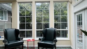 Une véranda avec deux fauteuils en cuir, une petite table rouge et un tapis noir.