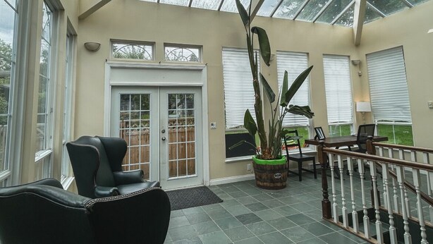 Une véranda avec un toit en verre, un fauteuil en cuir noir, une table en bois et une grande plante en pot.
