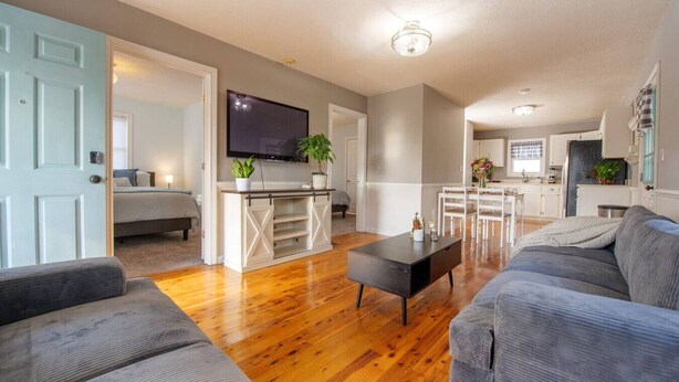 Una sala de estar moderna con sofá, mesa de centro y televisor. Hay una zona de cocina con mesa y sillas.