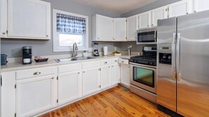 Una cocina moderna con gabinetes blancos, electrodomésticos de acero inoxidable, horno empotrado y microondas.