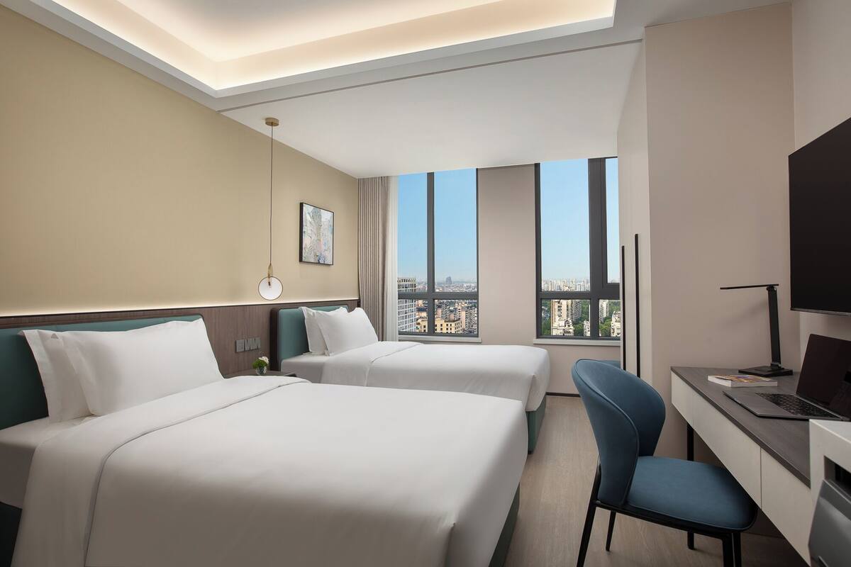 A hotel room with two beds, a desk, a chair, and a TV.