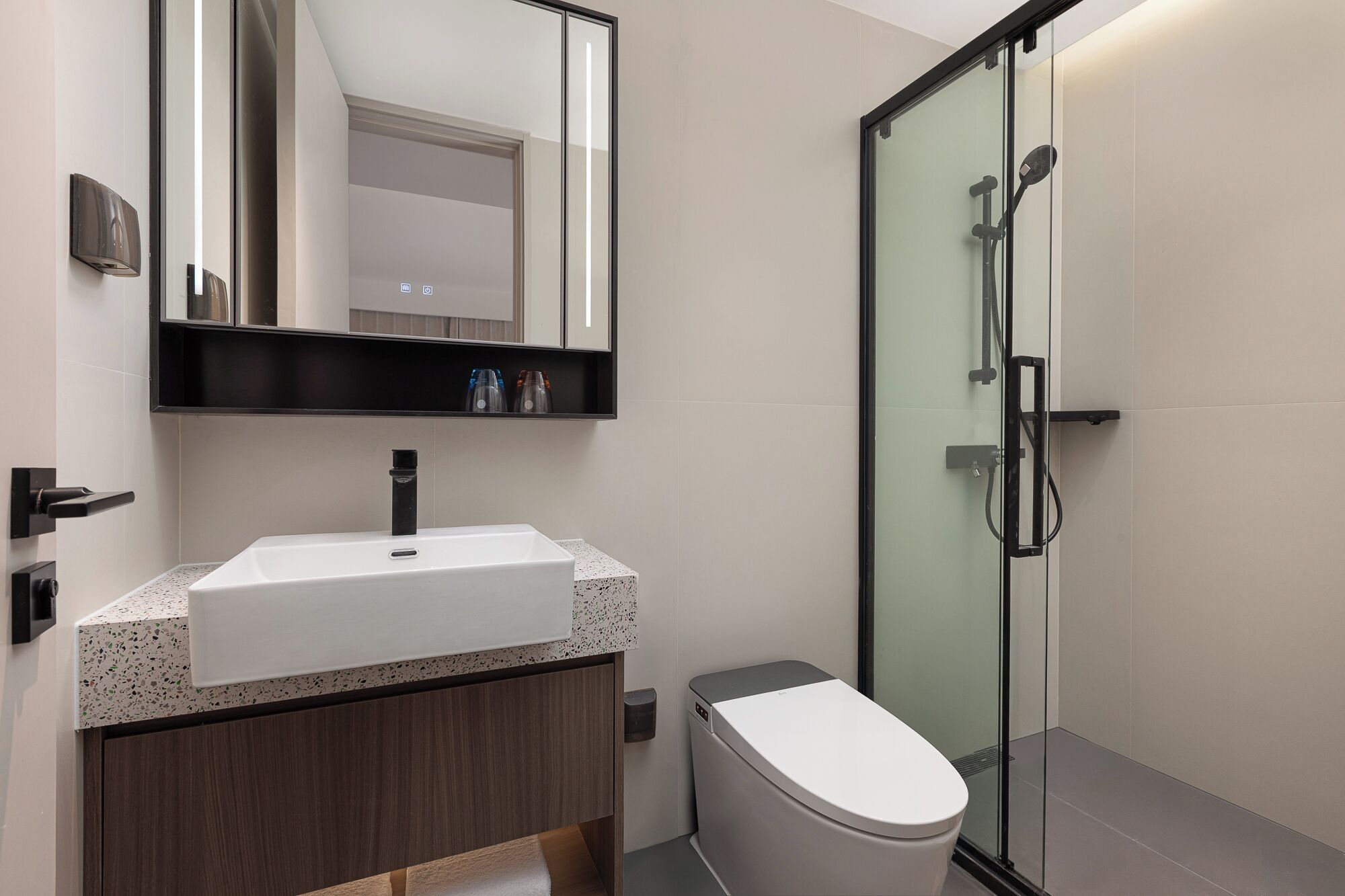 Une salle de bain moderne avec un lavabo blanc, un meuble-lavabo en bois foncé, une cabine de douche en verre et des toilettes.