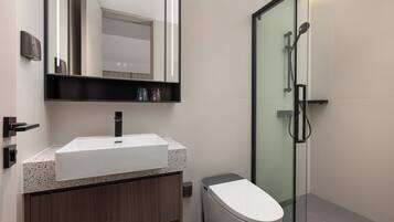 Une salle de bain moderne avec un lavabo blanc, un meuble-lavabo en bois foncé, une cabine de douche en verre et des toilettes.