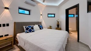 Ein modernes Schlafzimmer mit einem großen Bett, einem Deckenventilator und zwei Wand-Fernsehern.