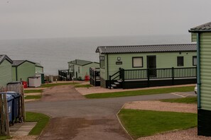 A row of green mobile homes with a paved path leading to a gate.