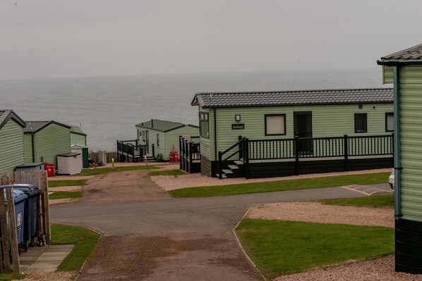 A row of green mobile homes with a paved path leading to a gate.