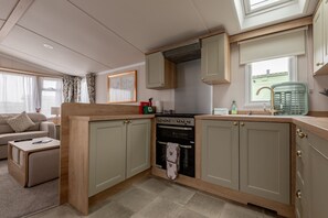 Une cuisine compacte avec des meubles en bois, un four encastré et une fenêtre donnant sur une maison.