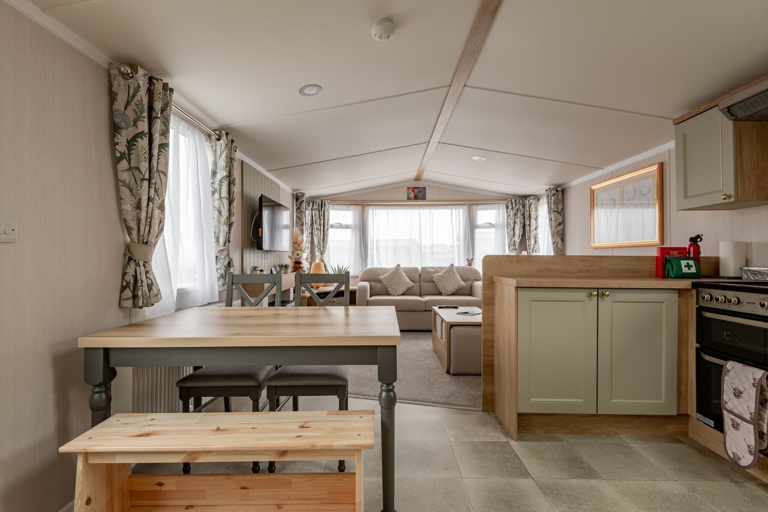 A compact kitchen with a dining area, a sofa, and a TV in the background.