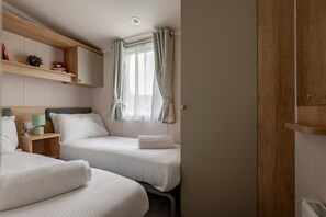 Une chambre avec deux lits, des têtes de lit en bois, une table de chevet avec une lampe et une fenêtre avec des rideaux.