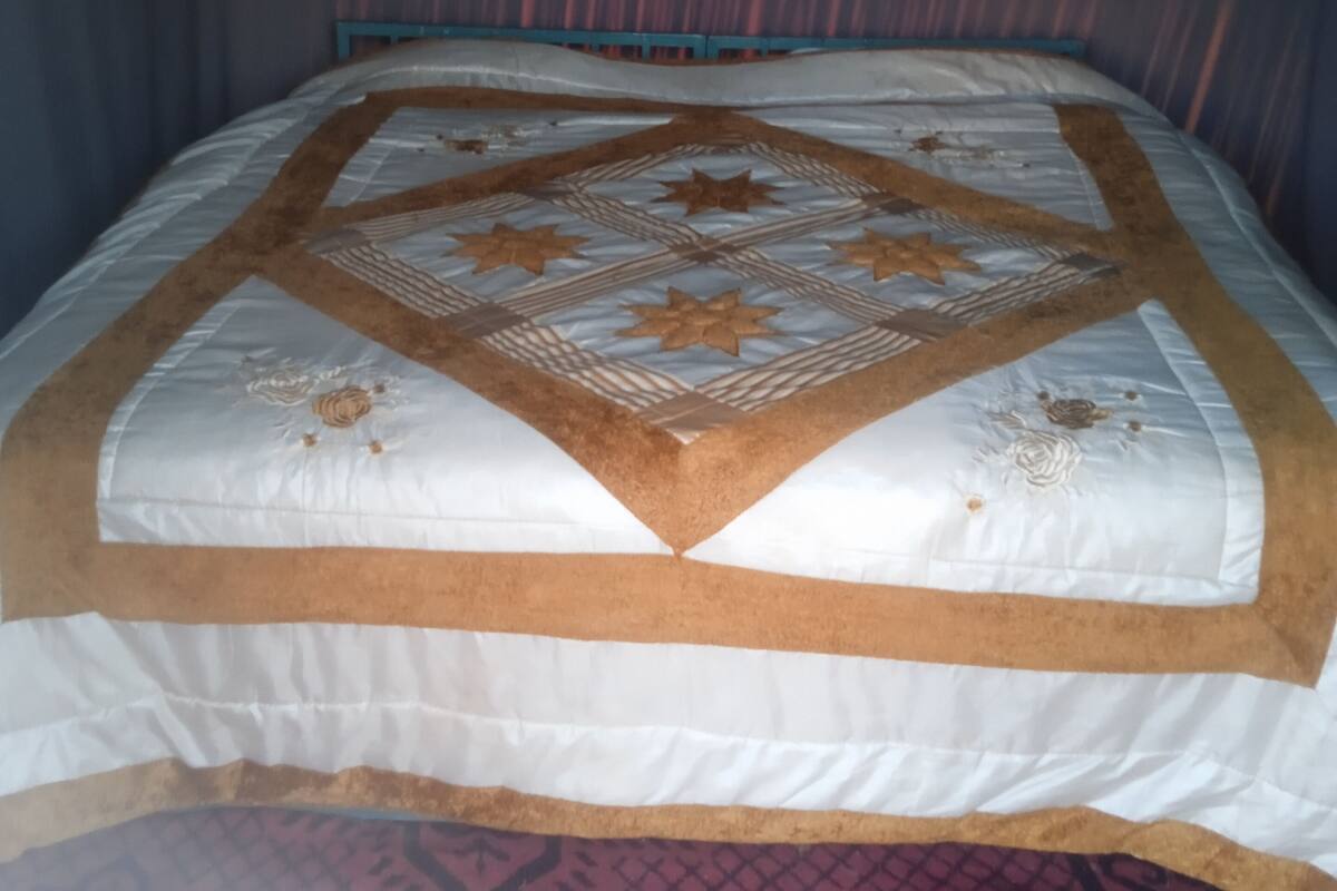 A bed with a patterned bedspread and a red patterned rug.