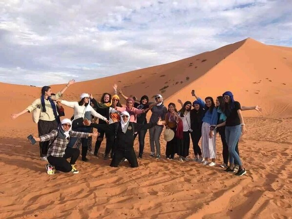 A group of people posing in a desert landscape with sand dunes in the background. - Sahara Merzouga Camp (Hassilabied)
