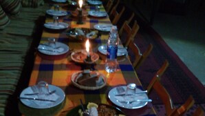 A long dining table set with plates, cutlery, candles, and a bottle of water. - Sahara Merzouga Camp (Hassilabied)