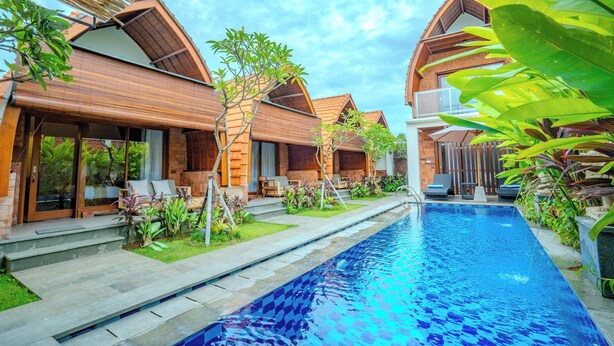 A poolside area with wooden buildings, outdoor seating, and a clear blue pool. - Villa Radha Pererenan (Pererenan)