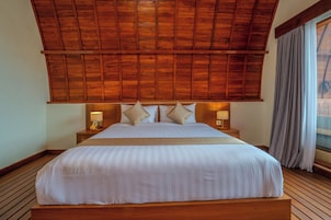 A large bed with a wooden headboard, two bedside lamps, and a view of the outdoors through a window with curtains.